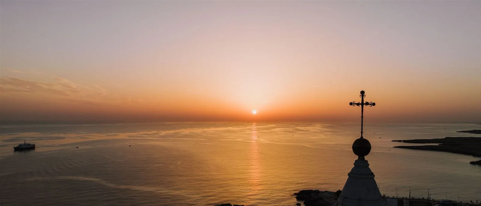 Alba sul mare Adriatico con la croce della cattedrale di Monopoli in controluce
